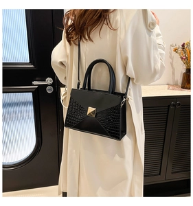 Detail of black faux crocodile leather crossbody bag with golden pyramid clasp and handle