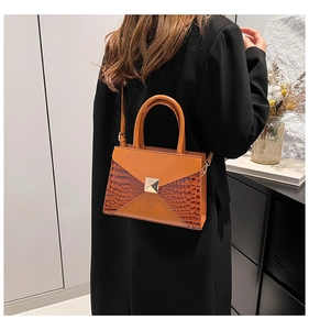 Model view of an orange crocodile pattern handbag styled with a long black coat