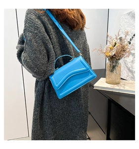 Blaue Umhängetasche mit gewellter Klappe an einem Model mit grauem Strickpullover