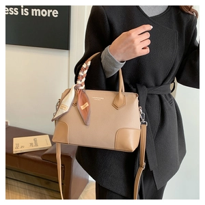 Dettaglio della borsa in pelle beige con manico in foulard di seta su panca moderna