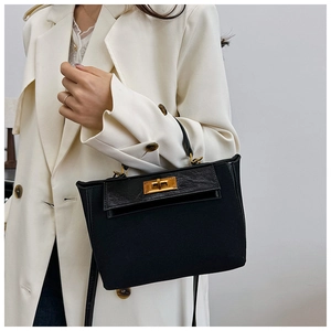 Detail of a vintage black canvas Kelly-style handbag with gold hardware on a white suit
