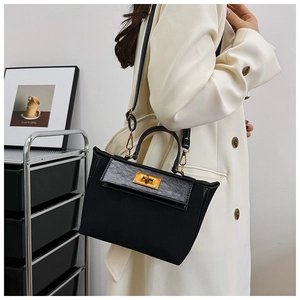 Detailed side view of a black vintage handbag with golden twist lock on a beige coat