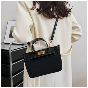 Detail view of black canvas and leather bag with gold metal clasp on a model