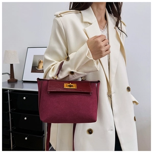 Detail view of burgundy tote bag featuring a gold metal lock and matte texture finish