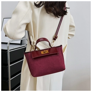 Detail of burgundy crossbody bag featuring a golden twist lock and suede texture contrast