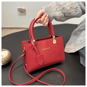 Close-up of a red leather tote bag with gold logo text and pleated accordion side details