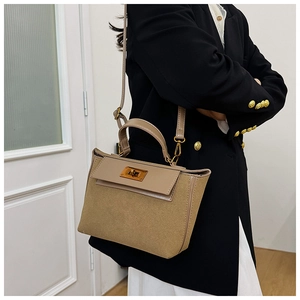 Close-up of khaki suede handbag with gold clasp detail worn with black blazer