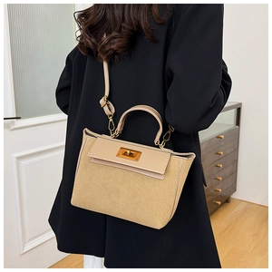 Detail of warm beige suede handbag featuring golden twist lock and adjustable strap on model