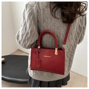 Close-up of a red leather crossbody bag with gold text lettering on a gray sweater backdrop