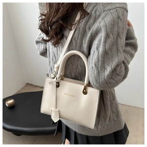 Detail of white PU leather crossbody bag with gold Fashion & Bags lettering on textured surface