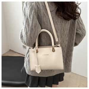 Detail of a beige leather tote bag with dual handles and gold hardware on a grey sweater