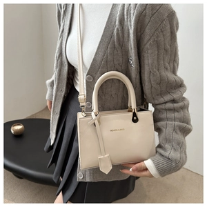 Close-up of beige leather handbag with gold 'FASHION & BAGS' text and top handle detail