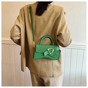 Détail d'un sac bandoulière vert avec boucle dorée en D et rabat à paillettes texturées