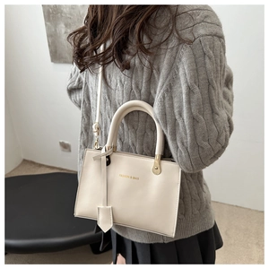 Detail showing the cream-white leather handbag with gold FASHION & BAGS lettering and hardware