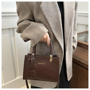 Brown leather crossbody square bag with gold FASHION & BAGS lettering on a textured coat
