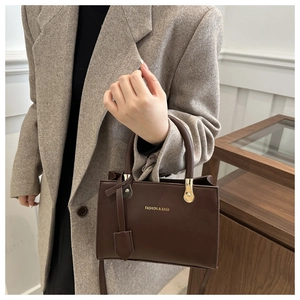 Detail of dark brown leather handbag featuring gold hardware and logo on textured coat