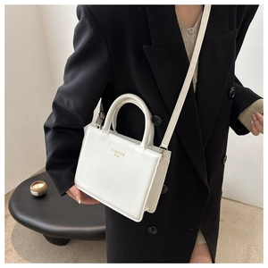 Detail of white square handbag featuring gold Fashion Bag text and adjustable strap