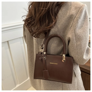 Detail of a dark brown leather Boston bag carried by a model wearing a grey wool coat