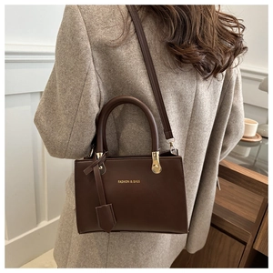 Lifestyle shot of dark brown leather handbag featuring gold logo and adjustable strap
