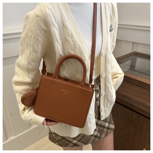 Detail of a brown leather square handbag with round coin purse and gold fashion logo