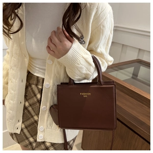 Close-up of a dark brown square leather handbag with gold Fashion Bag text on a model