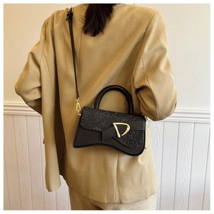 Détail d'un sac à main sablier noir avec paillettes et boucle D dorée sur un blazer