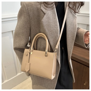 Beige Boston handbag with round handles and adjustable strap on a model in a gray suit