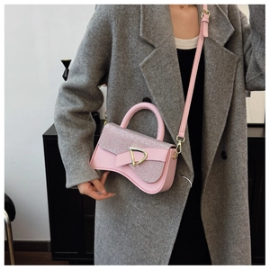 Sac à bandoulière rose pailleté avec boucle dorée porté par un mannequin en manteau