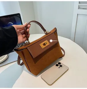 Detailed view of the brown suede handbag with golden turn-lock and leather handle