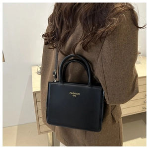 Structured black matte handbag with gold lettering shown on a model in a minimal setting
