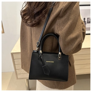Close-up of black leather handbag featuring gold FASHION & BAGS lettering and hardware