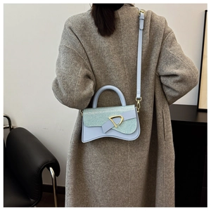 Détail d'un sac selle bleu clair avec boucle en D dorée sur une tenue en manteau gris