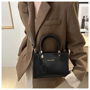 Detail view of black leather handbag with gold hardware and logo on model's shoulder