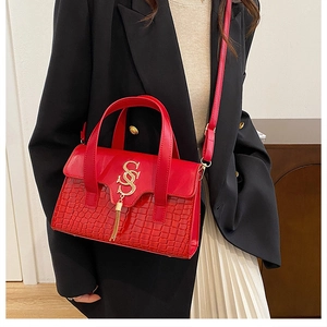 Detailansicht der roten Handtasche mit Krokodilmuster, goldener Quaste und S-Verschluss