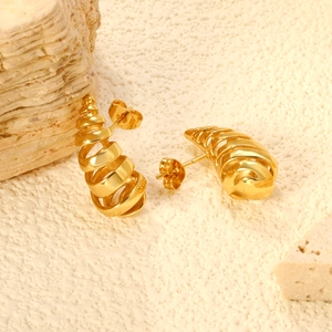 Golden spiral metal stud earrings with polished mirror finish on rustic stone background