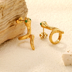 Golden snake stud earrings with green gemstone eyes on a natural stone background