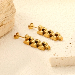 Detailed close-up of golden watch-band style geometric stud earrings on a stone background
