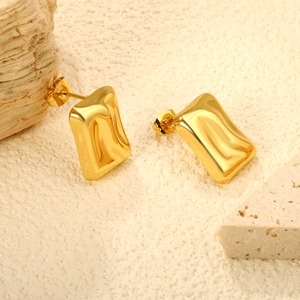 Close-up of golden rectangular stud earrings with liquid wave texture on stone background