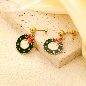 Golden Christmas wreath earrings with green enamel and red bow on a textured stone base