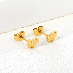 Close-up of polished 18K gold plated butterfly stud earrings on textured white surface