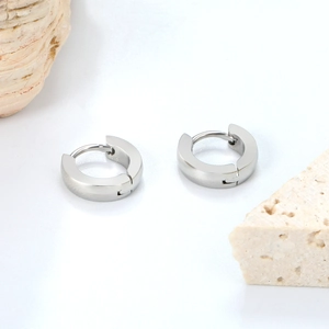 Close-up of polished silver stainless steel hoop earrings on natural stone props