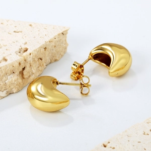 Macro shot of polished gold-plated curved stud earrings on white stone props