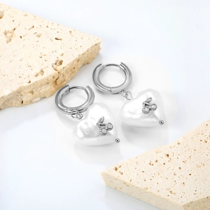 Détail de boucles d'oreilles cœur cerise avec finition argent et pendentif blanc