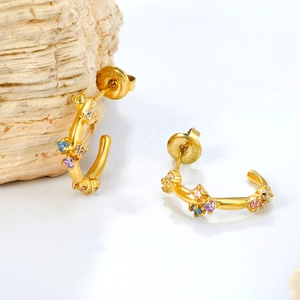 Goldene C-förmige Edelstahlohrringe mit bunten Zirkoniasteinen auf Muschelhintergrund