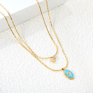 Double layered gold chain necklace with blue evil eye pendant and round crystal charm