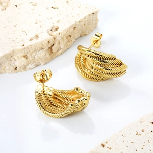 Macro detail of twisted gold metal earrings on a natural stone textured background