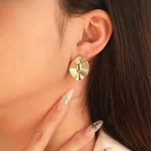 Close-up of vintage golden textured oval earrings worn by a model in natural light