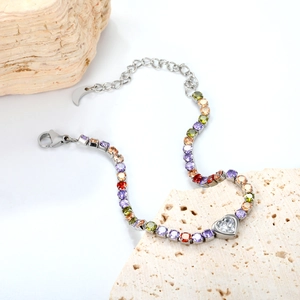 Colorful zircon heart bracelet in stainless steel displayed on beige stone props
