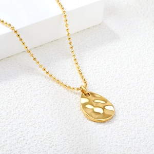 Hammered gold oval drop pendant necklace with bead chain on geometric white display