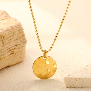 Macro detail of 18K gold plated hammered circular pendant on a classic ball chain necklace